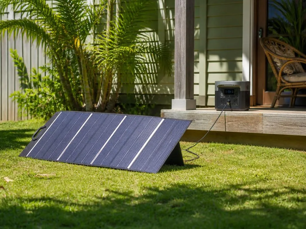 Painel solar portátil aberto no quintal ensolarado, conectado à estação de energia na varanda